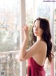 A woman in a red dress standing by a window.