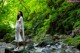 A woman standing on a rock in the middle of a stream.